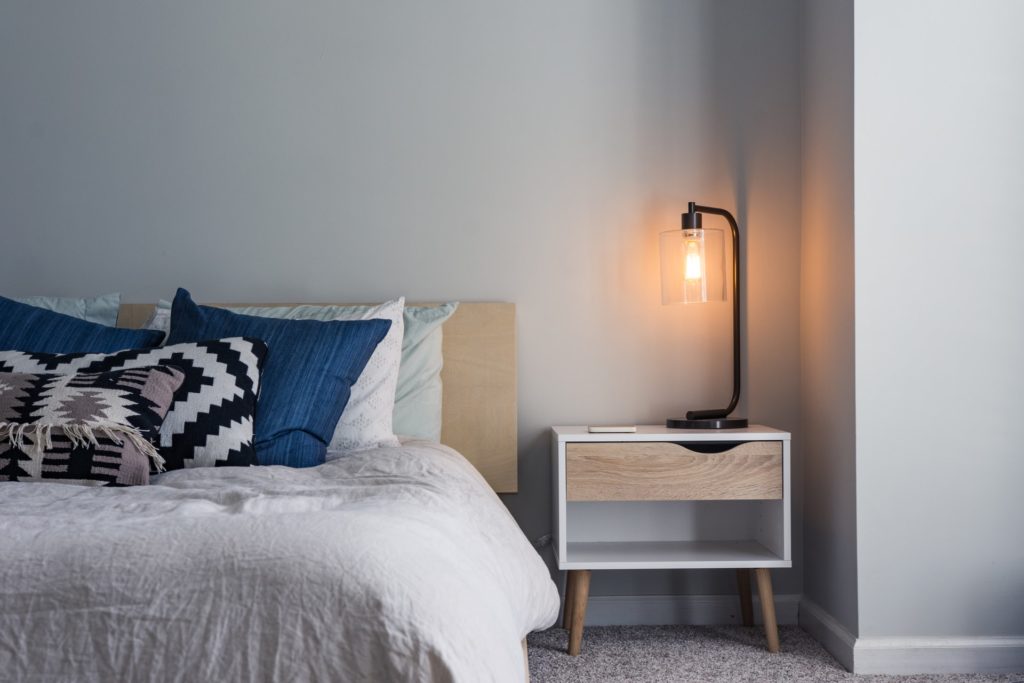 lit une personne avec chevet bois, lampadaire design et coussins géométriques dans une chambre minimaliste