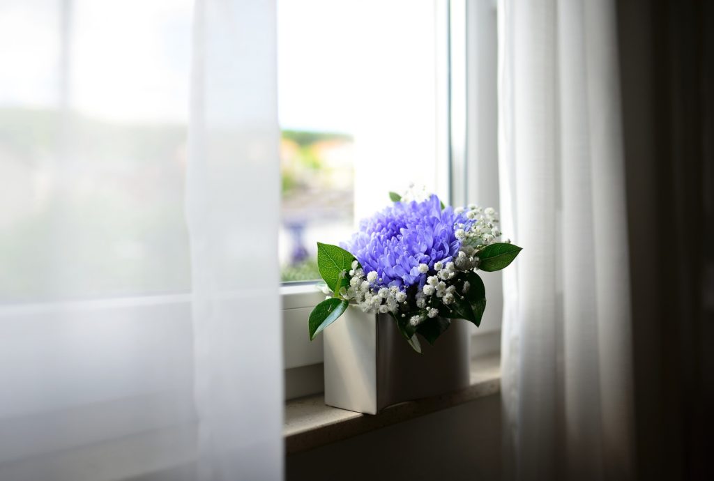 fleurs violettes et blanches dans vase blanc sur windowsill avec rideaux légers