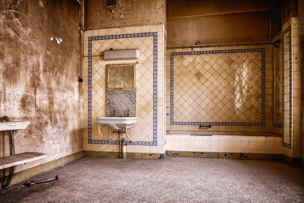 salle de bain abandonnée avec carrelage bleu et blanc usé, miroir et lavabo délabrés