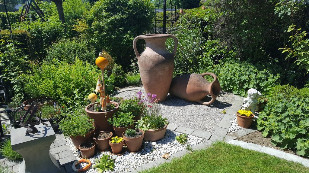 jardin zen avec urnes terracotta, plantes en pots et galets blancs