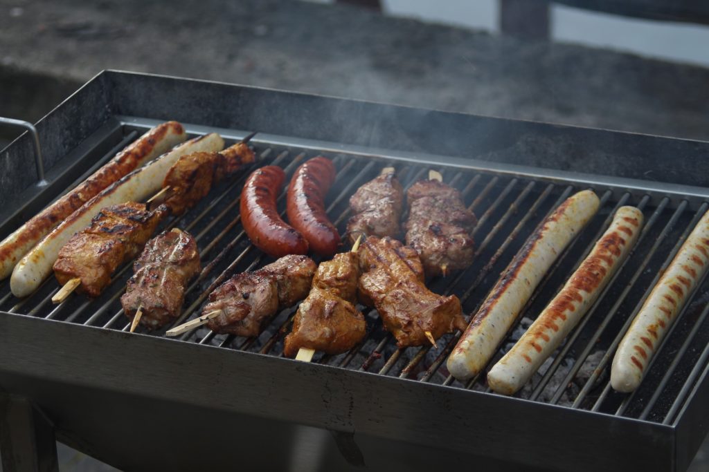 barbecue avec viandes, saucisses et brochettes en cours de cuisson sur grille