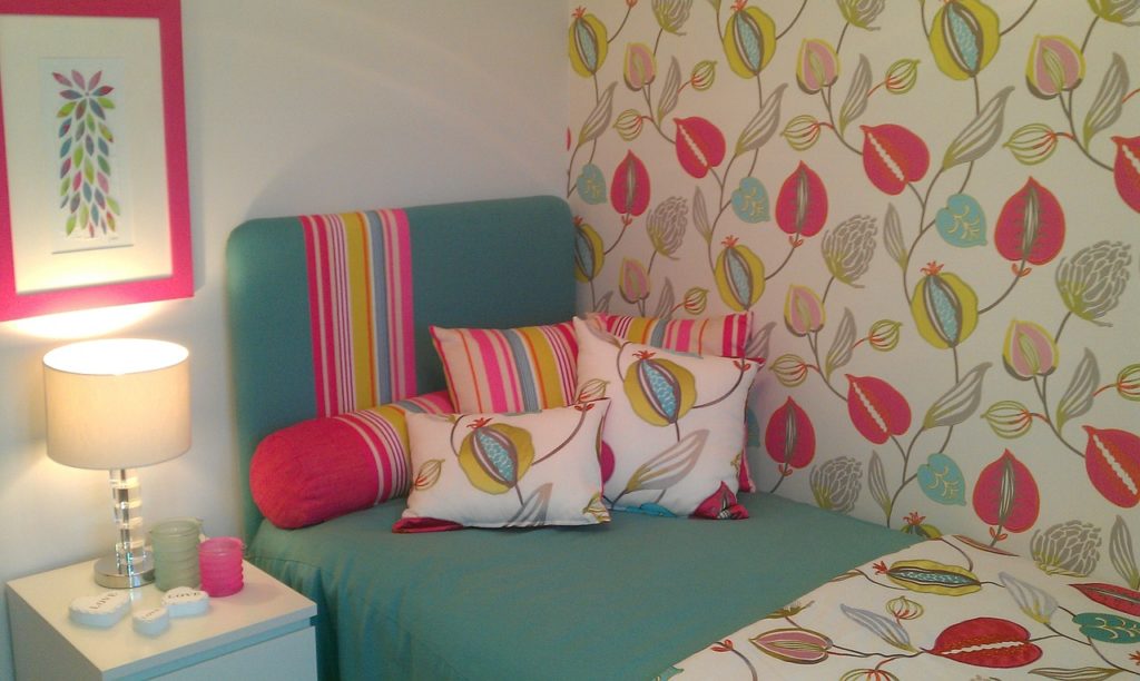 chambre colorée avec papier peint floral, lit turquoise et coussins rayés