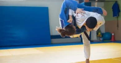 Two judokas practicing a powerful throw during judo training indoors on tatami mats.
