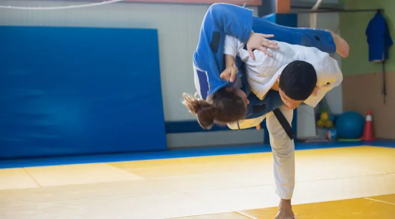 Two judokas practicing a powerful throw during judo training indoors on tatami mats.