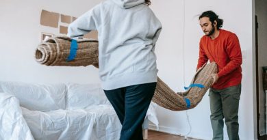 A couple unrolls a carpet in their new apartment, amidst moving and unpacking.